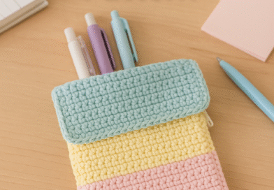 Handmade crochet stationery case in pastel colors with zipper, placed on a desk with pens inside,