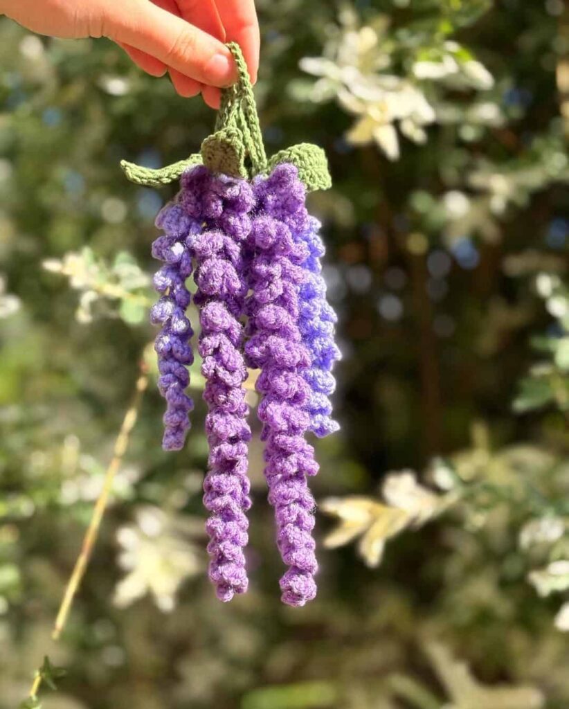 Crochet wisteria pattern finished flower strand in purple ombre held in hand outdoors