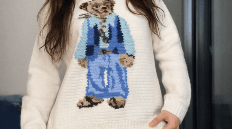 Woman wearing a cream crochet sweater featuring a Polo Bear design, styled with blue jeans and photographed indoors.