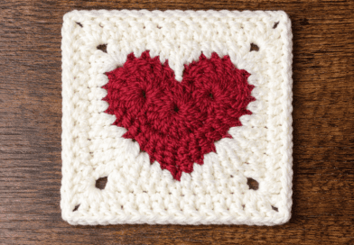 Crochet heart granny square pattern with red heart center and white border displayed on a wooden background