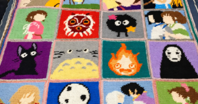 Handmade anime crochet blanket with pixel-style character squares, Ghibli inspired design, black borders and vibrant colorwork panels displayed on wooden floor.
