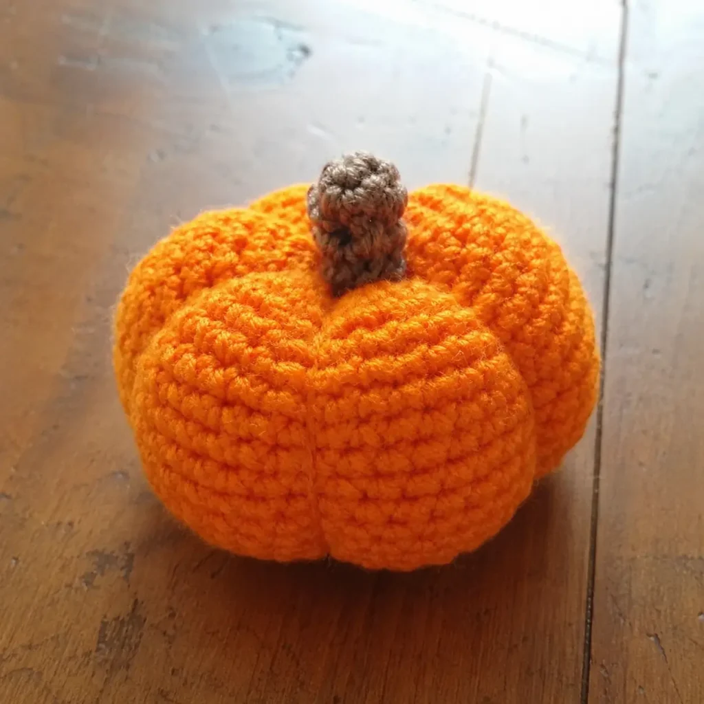 Crochet pumpkin pattern free — finished orange amigurumi pumpkin with brown stem on wooden table