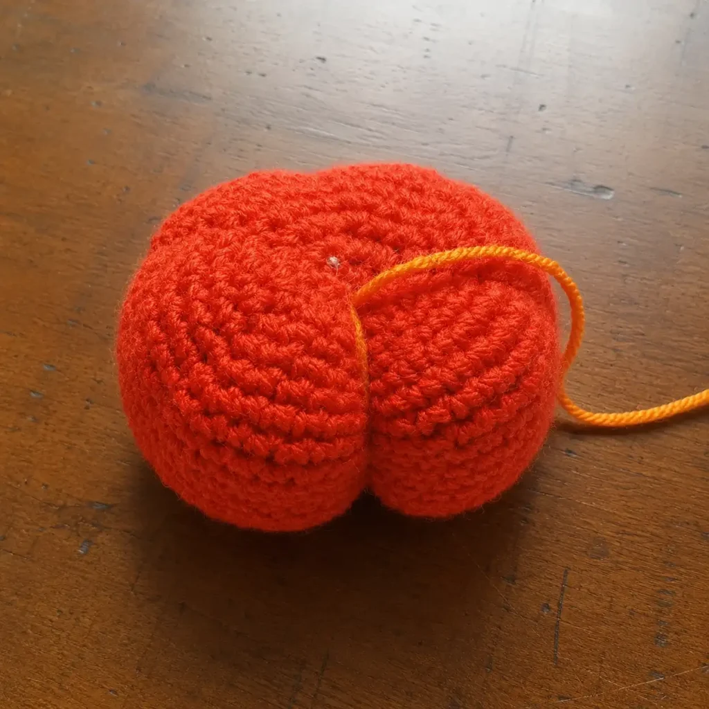 Crochet pumpkin pattern free — first ridge cinched showing how the pumpkin shape begins to form